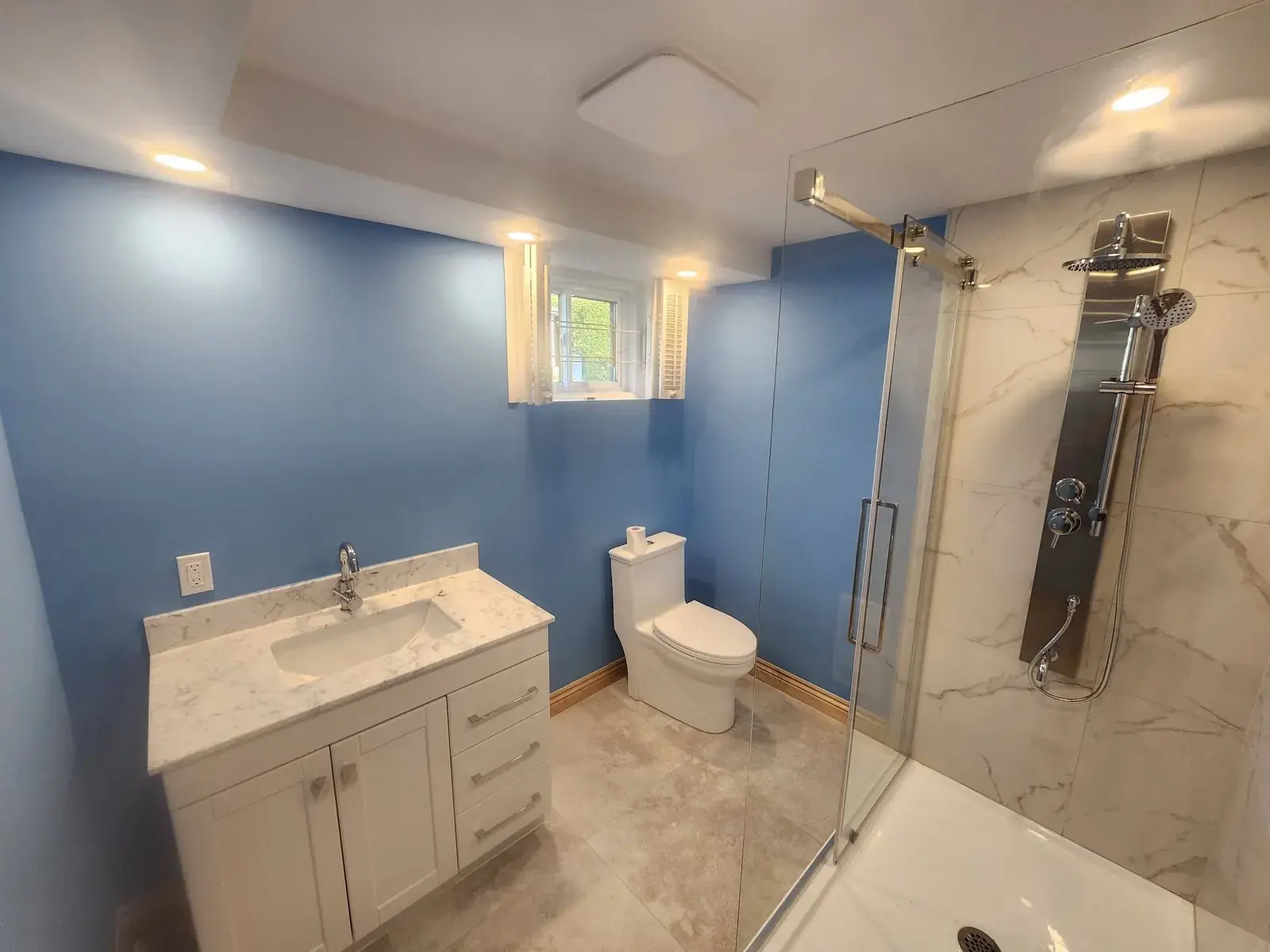 Salle de bain terminée avec douche vitrée, vanité et murs bleus